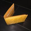 A yellow Genuine Ostrich Skin Leather Men's Bifold Wallet made in USA - Best Prices sitting on a black floor.